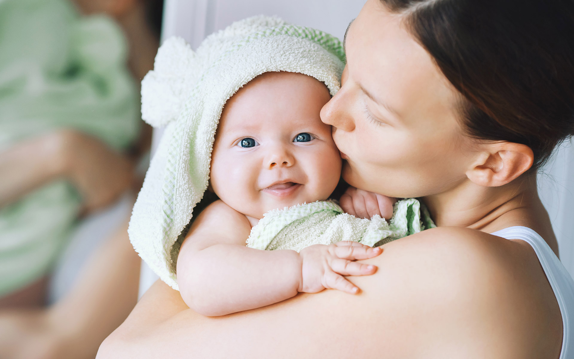 mother holding her new born child wrapped in a towel and kisses the baby