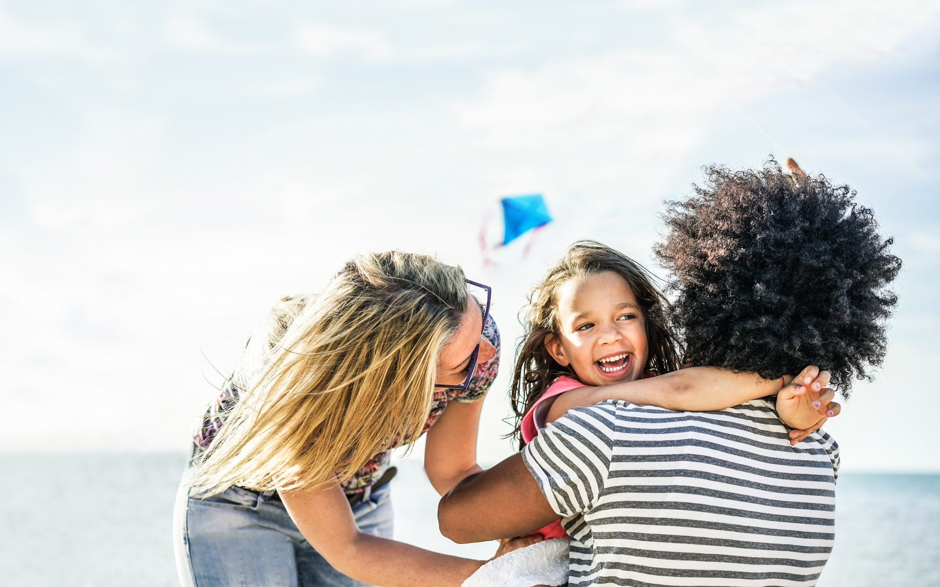 family hugging happily at a beach while kite flying